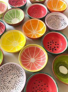 many different colored bowls with holes in them on a white table top and one has an orange slice cut out of it