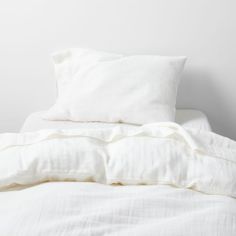 an unmade bed with white sheets and pillows