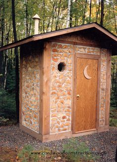 a small outhouse in the woods with a moon on it's roof and door