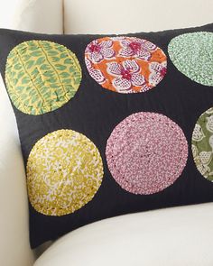 a black pillow with colorful circles on it sitting on a white chair in front of a wall