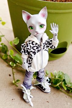 a white cat figurine standing next to a potted plant with green eyes