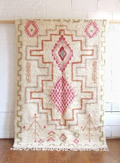 a white and red rug on top of a wooden floor next to a brick wall