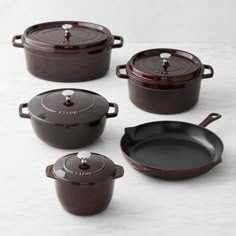 four cast iron pots and pans on a white countertop, with the lids off