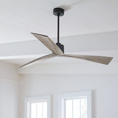 a ceiling fan in a white room with two windows