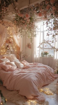 an unmade bed with pink sheets and flowers on the headboard is surrounded by fairy lights