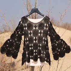 a black crocheted sweater hanging on a clothes rack in front of sand dunes