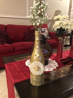 a table with vases and flowers on it in front of a red couches