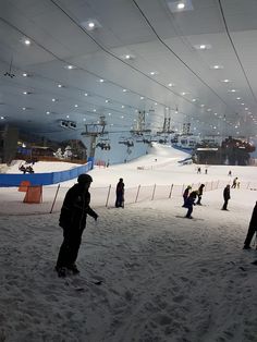 people are skiing and snowboarding in an indoor ski area at night time with lights on the ceiling