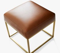 a brown leather ottoman with gold metal frame and footrests on an isolated white background