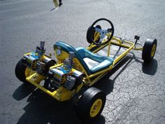 a small yellow and blue car sitting in the middle of a parking lot next to a person