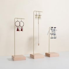 three pairs of earrings are on display in front of a white wall and two wooden stands