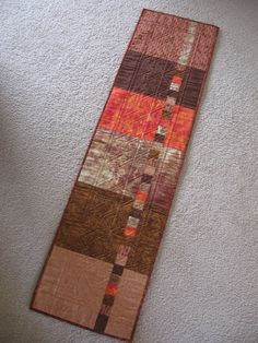 an orange and brown patchwork quilt laying on the floor next to a white wall