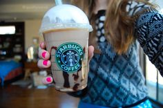 a woman holding up a starbucks drink in her right hand with chocolate sprinkles on it