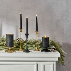 three candles on top of a mantle with pine cones and evergreen branches in the background