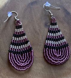 These handmade beaded earrings are truly unique. Each one is hand made with a rotating pattern. These earrings are available in a multitude of colors -making them perfect for any outfit! Whether it's dressing up a jean jacket or adding a unique texture to a LBD, there's no way you can go wrong with these earrings! We have given each design a name in honor of our favorite people! Unique Purple Earrings With Ear Wire, Traditional Purple Beaded Earrings For Festivals, Purple Teardrop Bohemian Earrings, Black Beaded Teardrop Earrings, Black Beads Teardrop Earrings, Purple Artisan Earrings With Ear Wire, Pink Beaded Earrings With Black Beads For Gift, Adjustable Teardrop Beaded Earrings With Black Beads, Purple Artisan Earrings With Dangling Beads