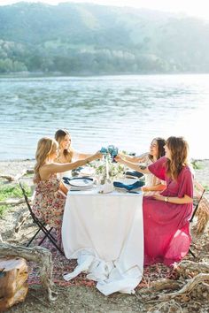 three women sitting at a table with plates and wine glasses in front of the water