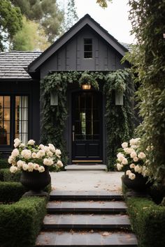 a black house with white flowers in front of it and steps leading up to the door