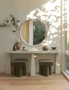 two stools sit in front of a table with a mirror and vase on it