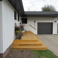 a wooden deck in front of a white house with flowers and plants on the steps