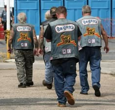 three men walking down the street with their backs to each other wearing leather vests