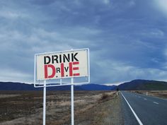 a drink drive sign sitting on the side of a road next to a dry grass field