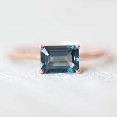 an emerald - cut blue topazte ring sits on a white surface in this close up photo