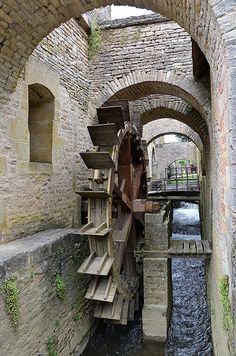 an old water wheel in the middle of a stone tunnel with steps leading up to it