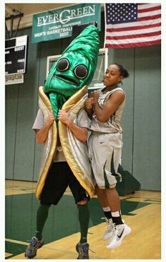 a man standing next to a giant green banana mascot on top of a basketball court