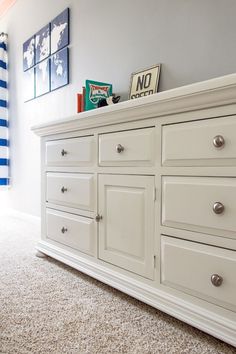 a white dresser sitting in a bedroom next to a wall with pictures on top of it