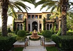 a large house surrounded by palm trees and greenery with a fountain in the middle