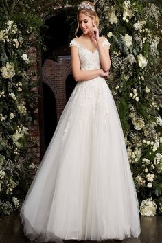 a woman standing in front of a flower covered wall wearing a wedding dress with flowers on it