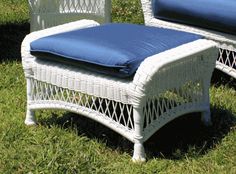 two white wicker chairs with blue cushions on the grass in front of some bushes