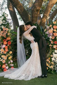 a bride and groom kissing in front of a floral arch at their outdoor wedding ceremony