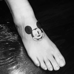 a mickey mouse tattoo on the foot of a person's left foot, which is black and white