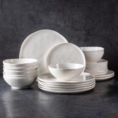 a stack of white plates and bowls sitting next to each other on a black surface