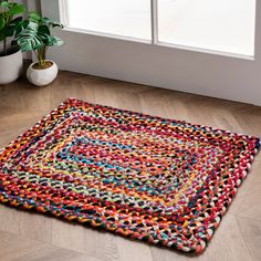 a multicolored rug on the floor next to a potted plant and window