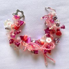 a bracelet made out of beads and other items on a white tablecloth with a pair of scissors in the middle