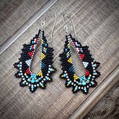 Tiny black, silver, red, blue, yellow and silver seed beads are woven around silver plated hand formed wire loops in a bold geometric pattern. The beaded earrings dangle from graceful sterling silver ear wires and are lightweight. Dimensions: 2.5 inches from the top of the ear wires to the bottom of the beadwork and 1.25 inches at the widest point. You can find more handmade earrings at https://www.etsy.com/shop/windyriver?section_id=5553062 Thank you! Artisan Black Beaded Drop Earrings, Silver Beaded Earrings With Colorful Beads For Festival, Artisan Black Beaded Earrings With Ear Wire, Festival Black Beaded Drop Earrings, Adjustable Multicolor Earrings With Silver Beads, Silver Teardrop Beaded Earrings With Colorful Beads, Bohemian Black Earrings With Silver Beads, Southwestern Style Multicolor Jewelry With Black Beads, Artisan Black Beaded Dangling Earrings