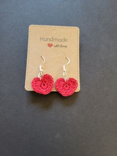 red crocheted heart earrings with silver hooks on black table next to small card