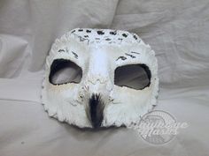 a white owl mask with black spots on it's face and eyes, sitting on a white sheet