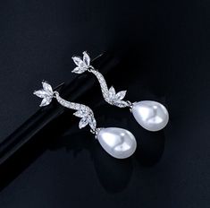 Romantic and elegant, this exquisite pair of earrings features iridescent white pearls and clear cubic zirconia that capture the light from every angle with a perfectly translucent appeal. The earrings are rhodium plated for a bright finish which enhances the intricate detailing and conveys a modern take on old elegance. Overall length of the earring is 38mm (approx. 1.5"). This exquisite design will add a touch of sophistication to any wedding gown or formal ensemble. Luxury Wedding Pearl Earrings With Lever Back, Luxury Sterling Silver Elegant Pearl Earrings, Luxury Elegant Pearl Earrings In Sterling Silver, Luxury Pearl Earrings With Elegant Design For Formal Events, Luxury Pearl Bridal Earrings With Elegant Design, Luxury Elegant Pearl Earrings For Wedding, Luxury Graceful Pearl Earrings For Formal Events, Luxury High Luster Pearl Earrings For Wedding, Luxury Elegant Pearl Bridal Earrings