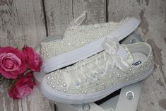 a pair of white sneakers sitting on top of each other next to pink flowers and scissors