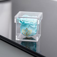 a clear box with a blue rose in it sitting on top of a table next to a mirror