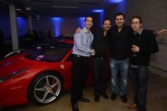 three men standing next to a red sports car