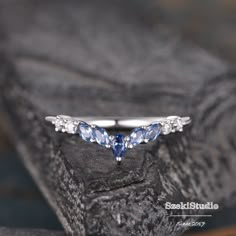 a white gold ring with blue sapphires and diamonds on the side, sitting on a rock