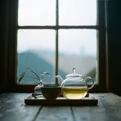 a tea pot and cup on a wooden table with a window in the background