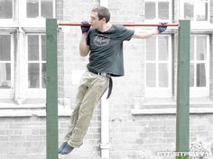 a man is doing pull ups on a bar in front of a brick building with windows