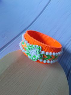 an orange bracelet with white beads and flowers on it sitting on top of a wooden table