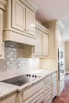 a kitchen with white cabinets and marble counter tops