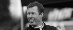 a black and white photo of a man in a racing suit smiling at the camera